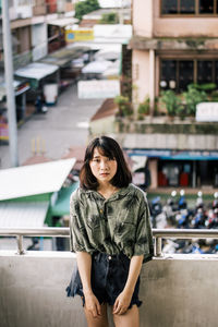 Portrait of young woman standing by railing