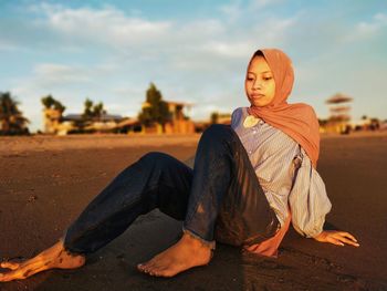 Portrait of young woman sitting on land against sky