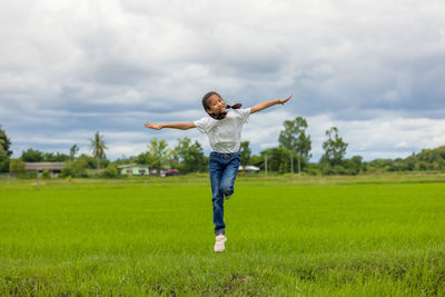 In an organic farmed rice field, happy asian children jumping raise their hands to the sky and grin.