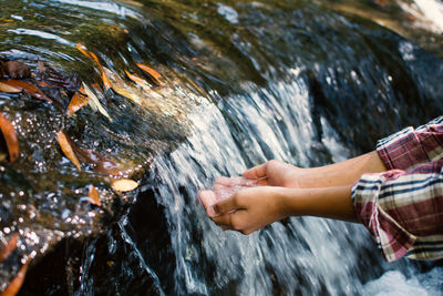 Cropped image of person with hands cupped by waterfall