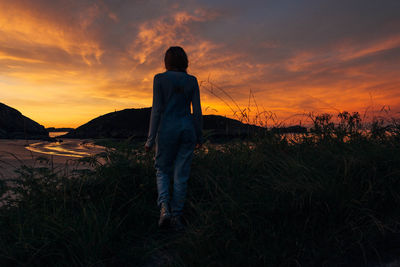 Rear view of girl standing on field against sky during sunset