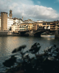 Bridge over river by buildings in city against sky