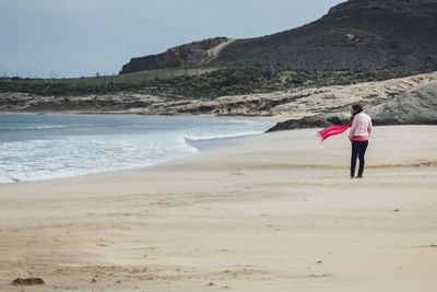 Rear view of woman standing on beach against sky