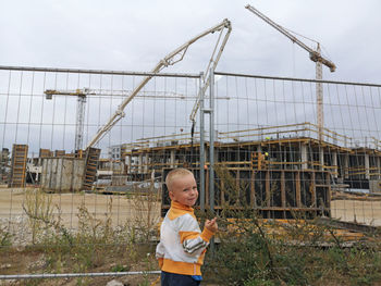 Girl standing by fence against sky