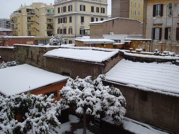 Snow covered houses against buildings in city