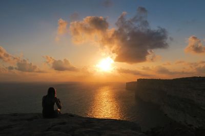 Rear view of woman sitting on beach against sky during sunset