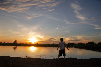 Rear view of man standing at beach during sunset