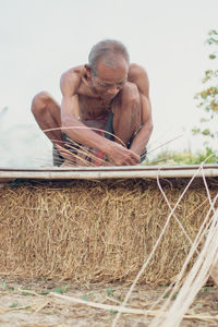 Shirtless senior man making straw basket