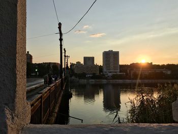River by buildings in city against sky during sunset