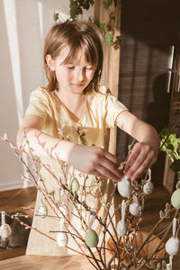  cute little girl hangs decorative textile easter eggs on a willow bouquet. bright holiday of easter