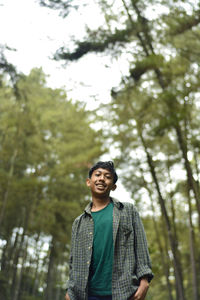 Low angle view of young man standing against trees