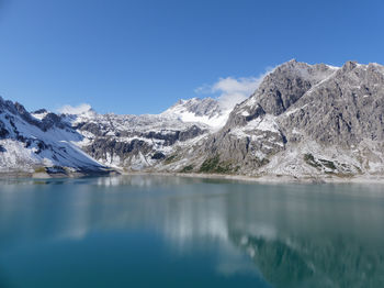 Scenic view of lake and snowcapped mountains against blue sky