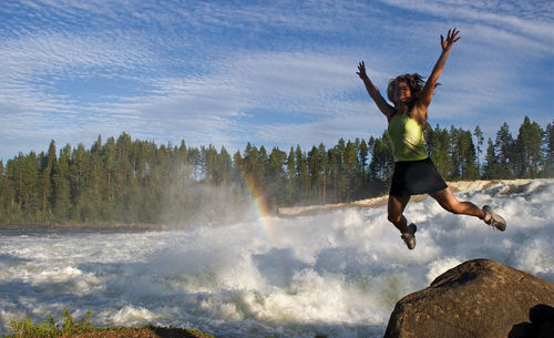 Full length of woman jumping on tree against sky