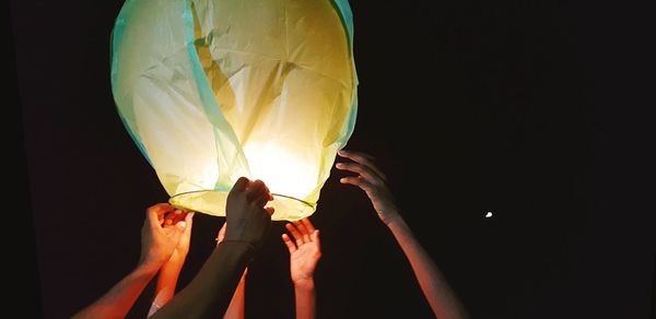 Cropped hands of people holding illuminated paper lantern against sky at night