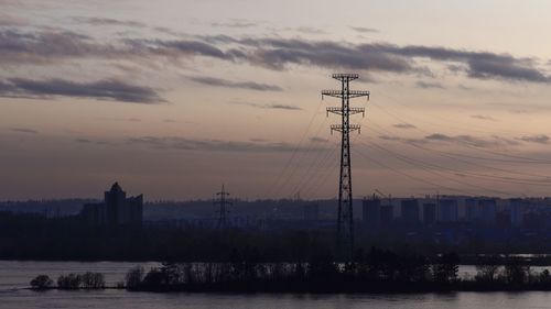 Silhouette electricity pylon by river against sky at sunset, angara river, irkutsk