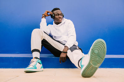 Full length of man sitting against blue wall