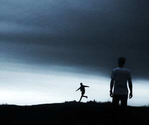 Men playing soccer on field against cloudy sky at dusk