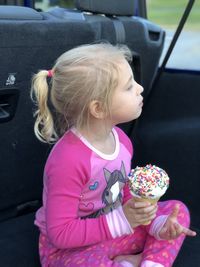 Girl eating ice cream while sitting in car trunk