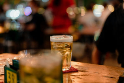 Image of a glass of beer on a wooden table in a tavern at night.