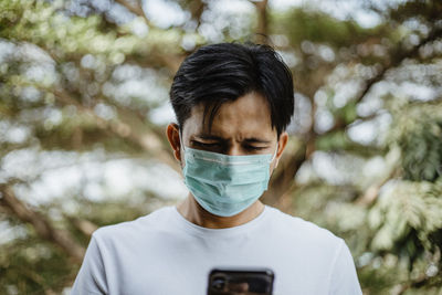 Man using mobile phone while wearing mask against trees