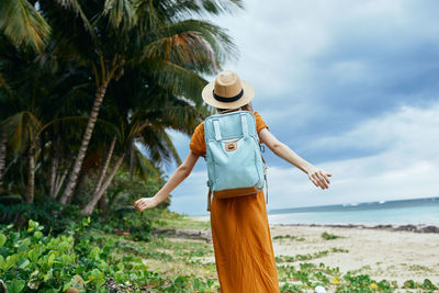 Woman standing by palm tree on beach against sky