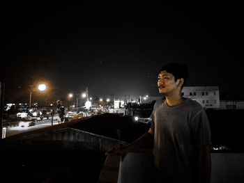 Young man looking at illuminated cityscape against sky at night