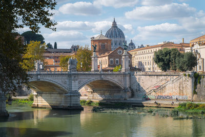 Arch bridge over river by buildings against sky