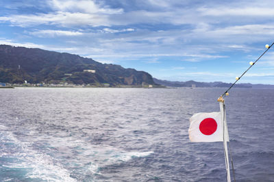 Japanese national flag waving along the uraga channel with the cliffs of the mount nokogiri