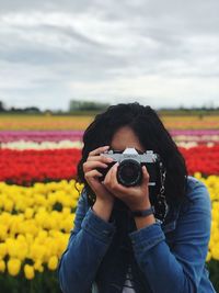 Portrait of woman photographing with camera on field against cloudy sky