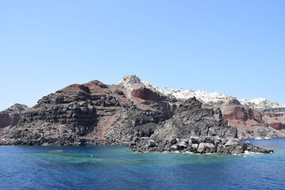 Rock formations in sea against clear blue sky