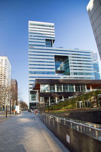 Road by buildings against clear blue sky