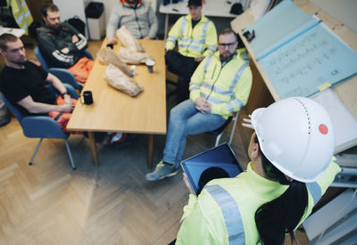 Female engineer with digital tablet discussing with male colleagues while planning together in office