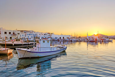 Boats moored in harbor at sunset