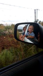 Portrait of man in car mirror against sky