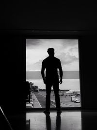 Silhouette man standing by window against sea