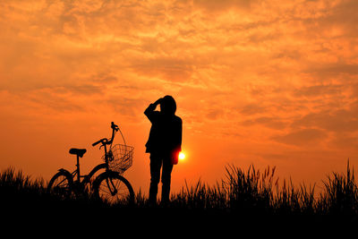 Silhouette person by bicycle against sky during sunset