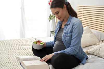 Pregnant woman eating salad while reading book