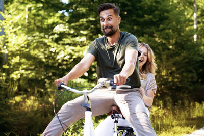 Happy couple sitting on bicycle against trees