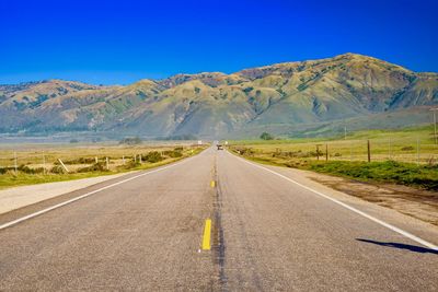 Road leading towards mountains against blue sky