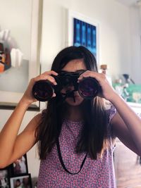 Portrait of girl looking through binoculars at home