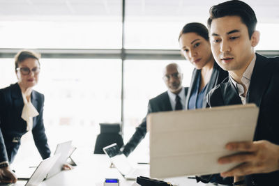 Young businessman explaining ideas to colleagues over digital tablet in conference room at office