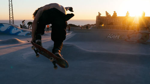 Man skateboarding in city against sky during sunset