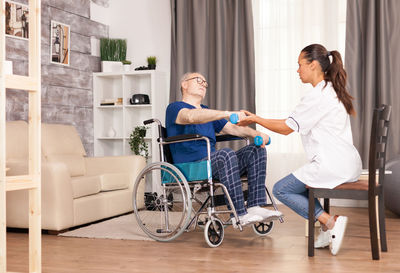 Female caretaker helping disabled man exercising at home