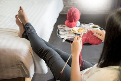 High angle view of woman knitting wool while sitting on sofa at home
