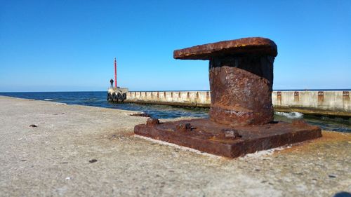 Close-up of rusty metallic structure on beach against clear blue sky
