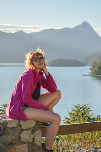 Midsection of woman sitting by lake against mountains