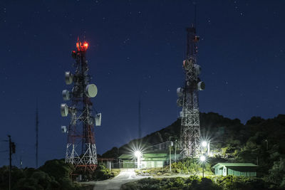 Low angle view of illuminated communications tower against sky at night