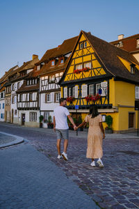 Rear view of people walking outside house against sky