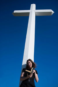 Low angle portrait of woman standing against blue sky