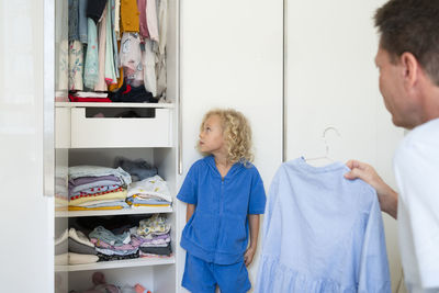 Father holding dress looking at daughter leaning on closet